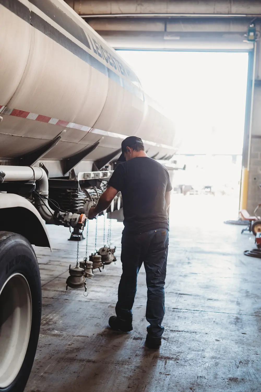 A technician working under a tanker trailer in an open bay door at Post Onsite