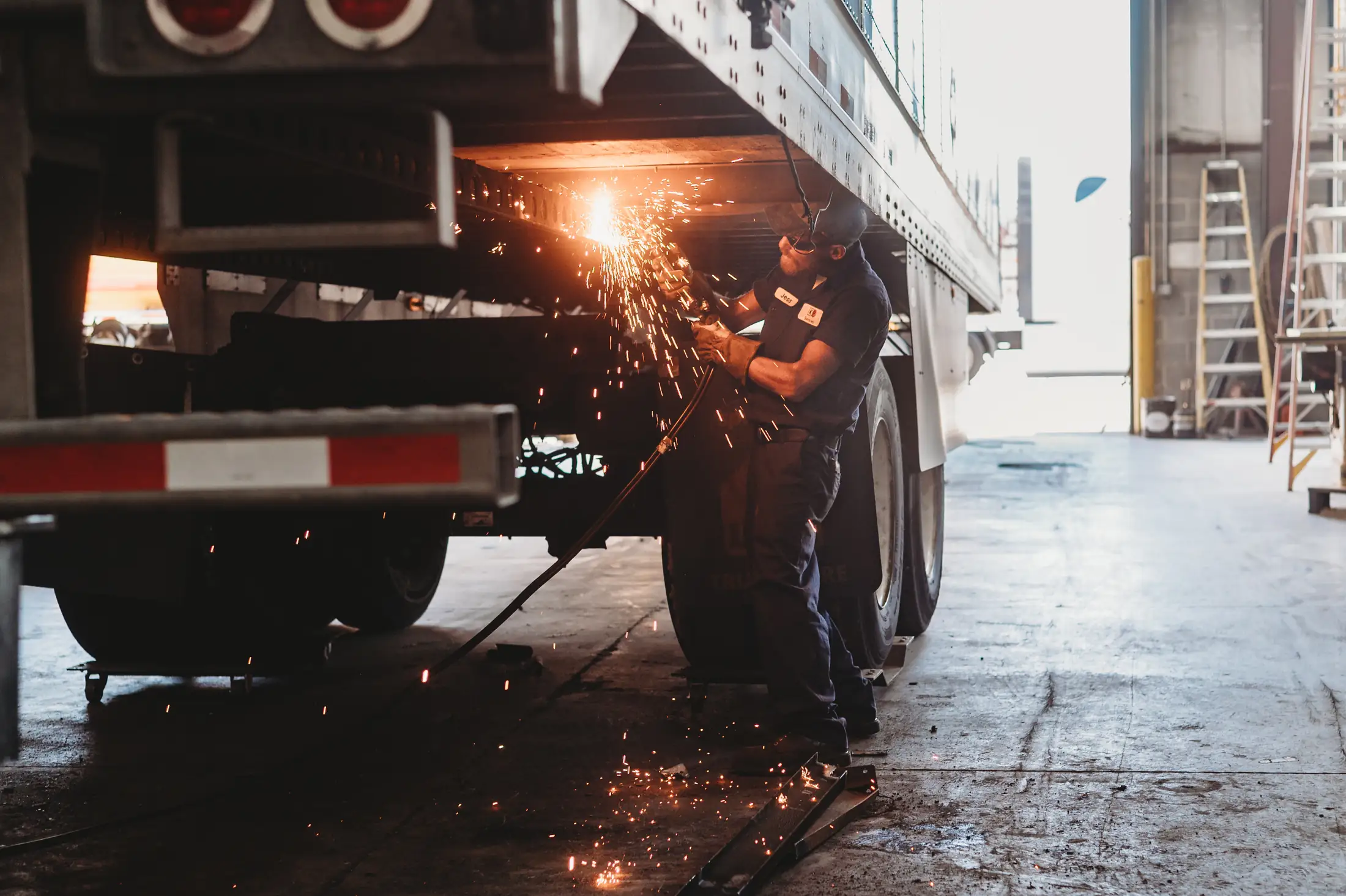 A technician grinding under a trailer at Knox Trailers, sparks across the bay floor